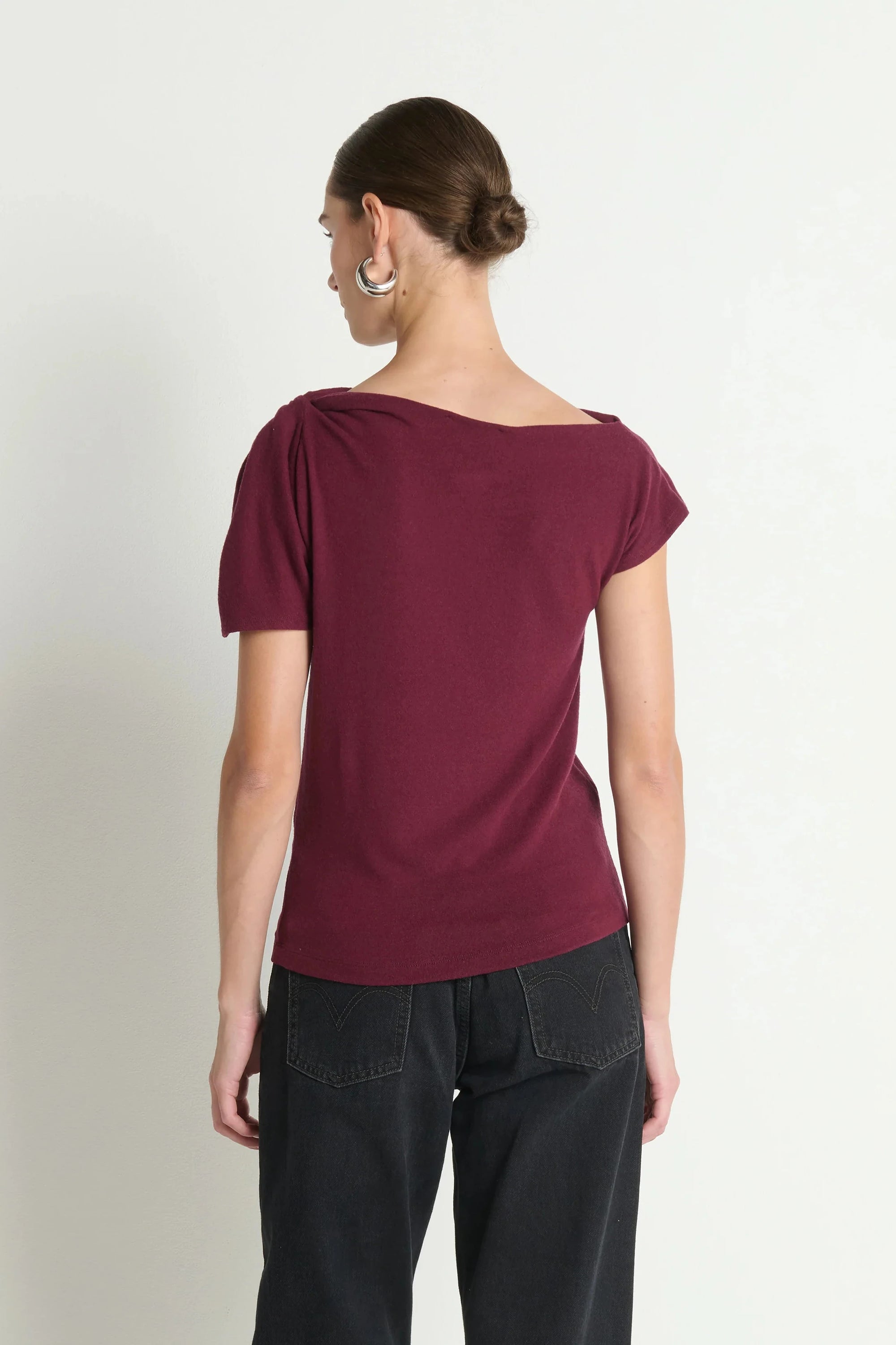 Woman wearing a burgundy top and black pants on a plain background