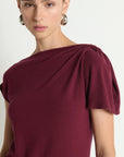 Woman wearing a burgundy dress with a draped shoulder design on a white background