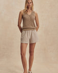 Woman wearing a beige sleeveless top and shorts against a beige background