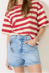 Person wearing a red and white striped shirt with blue denim shorts on a plain background