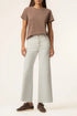 A model wearing a brown short-sleeve crewneck t-shirt, light gray wide-leg jeans, and dark brown lace-up sneakers, standing against a plain off-white studio background.