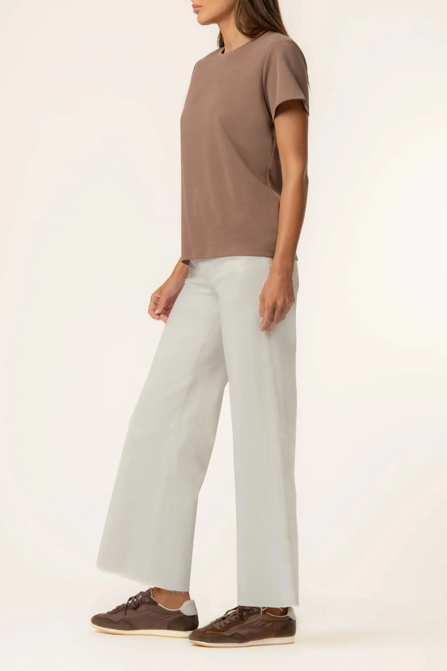 Person wearing a brown t-shirt and light gray pants on a white background