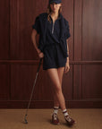 Person in navy outfit with cap holding a golf club against a wooden paneled wall.