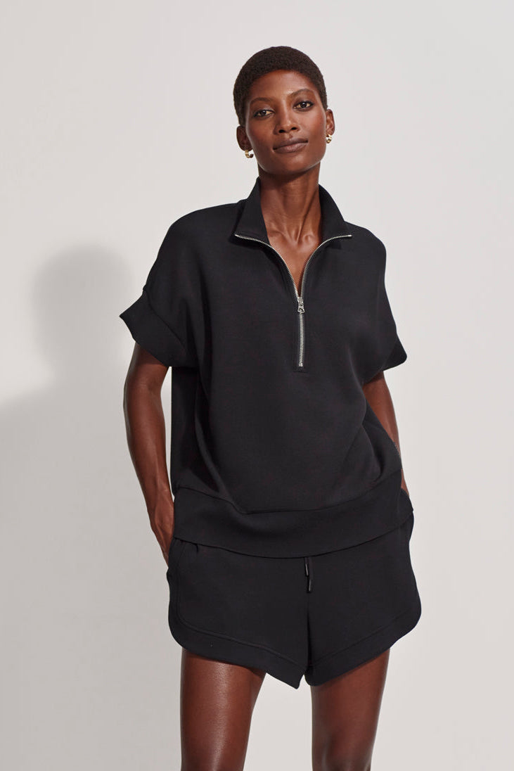Person wearing a black zip-up top and shorts on a plain background