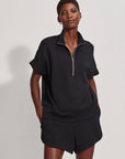 Person wearing a black zip-up top and shorts on a plain background