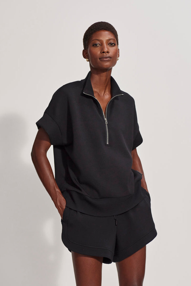 Person wearing a black outfit with a zip-up top and shorts on a white background