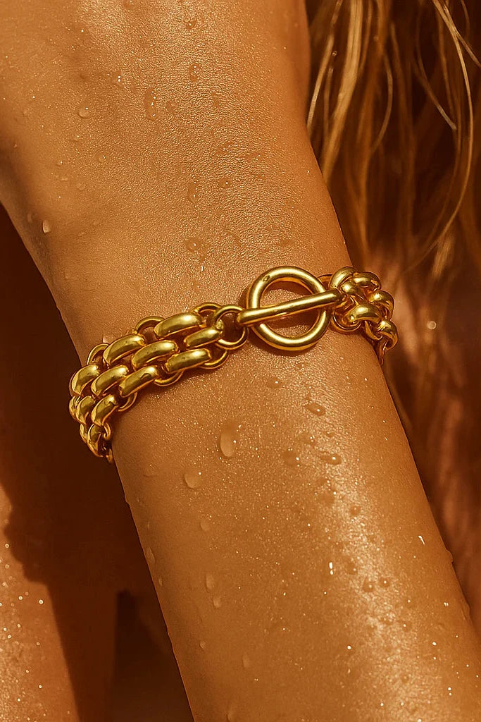 Gold chain bracelet on a sun-kissed arm with water droplets.