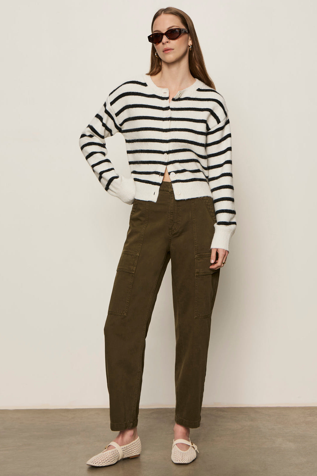 Woman wearing a black and white striped sweater and brown pants against a plain background