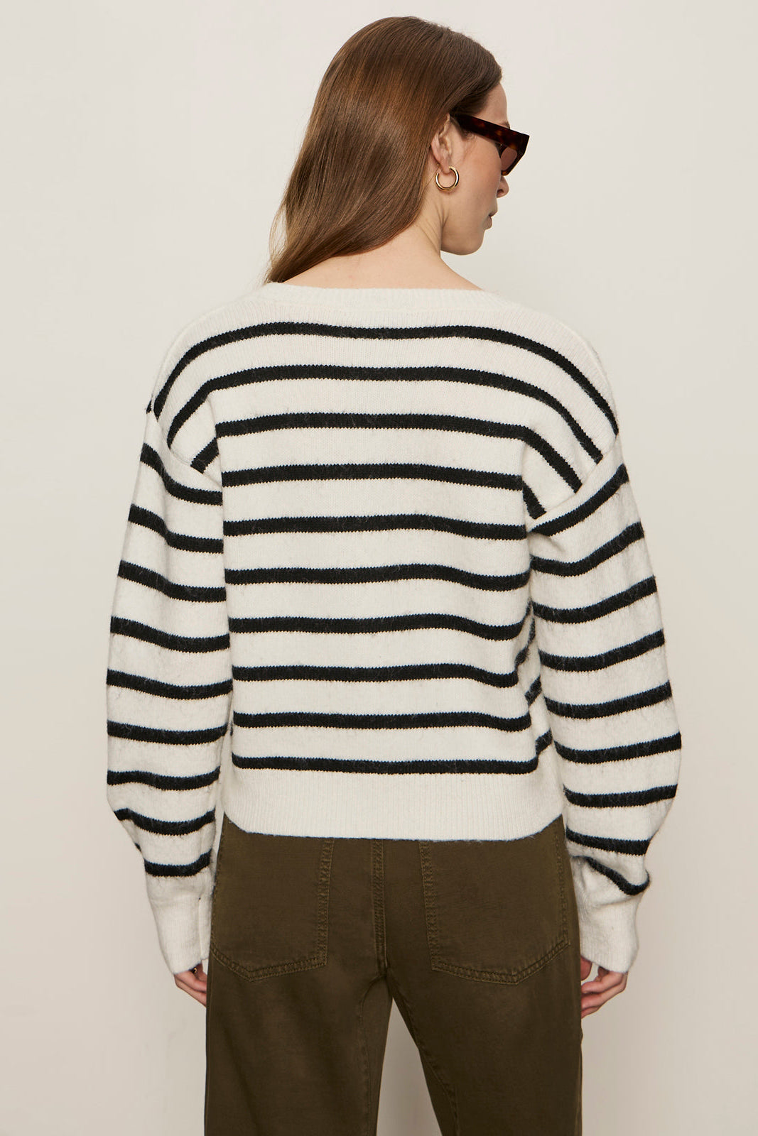 Person wearing a black and white striped sweater and brown pants on a plain background