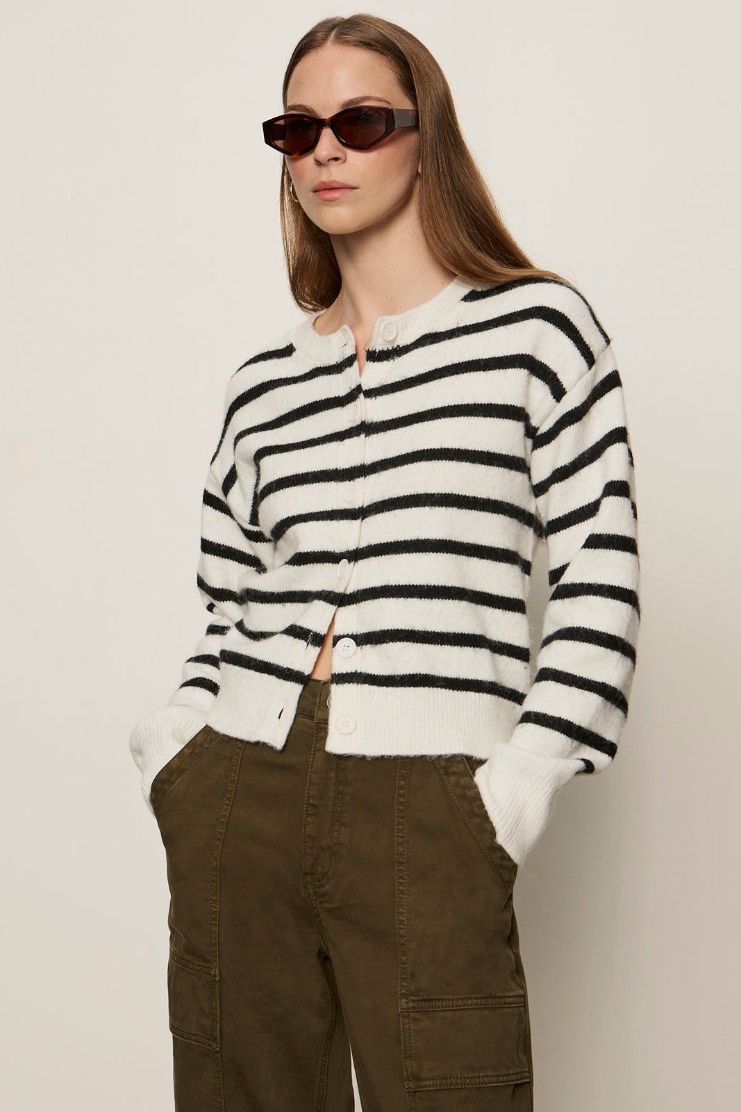 Woman wearing a black and white striped sweater and brown pants against a plain background
