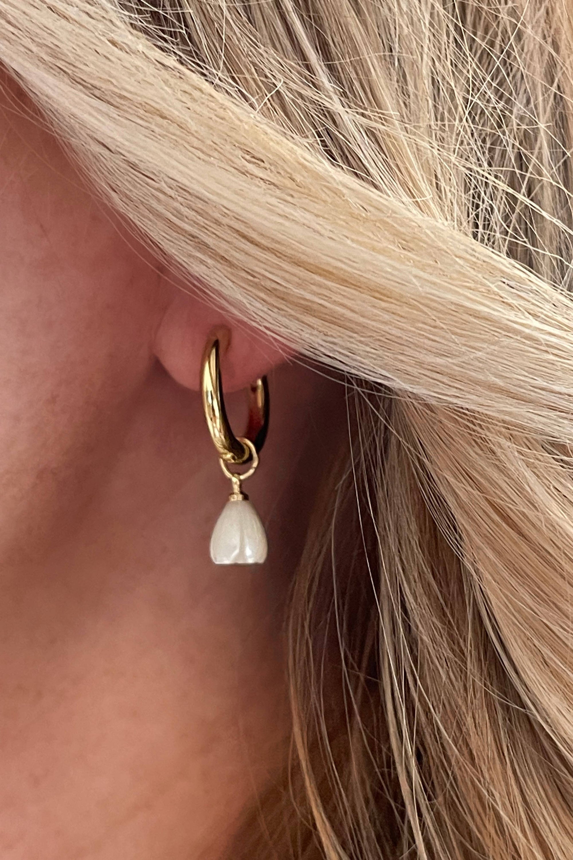 Close-up of a gold hoop earring with a pearl drop worn by a person with blonde hair.