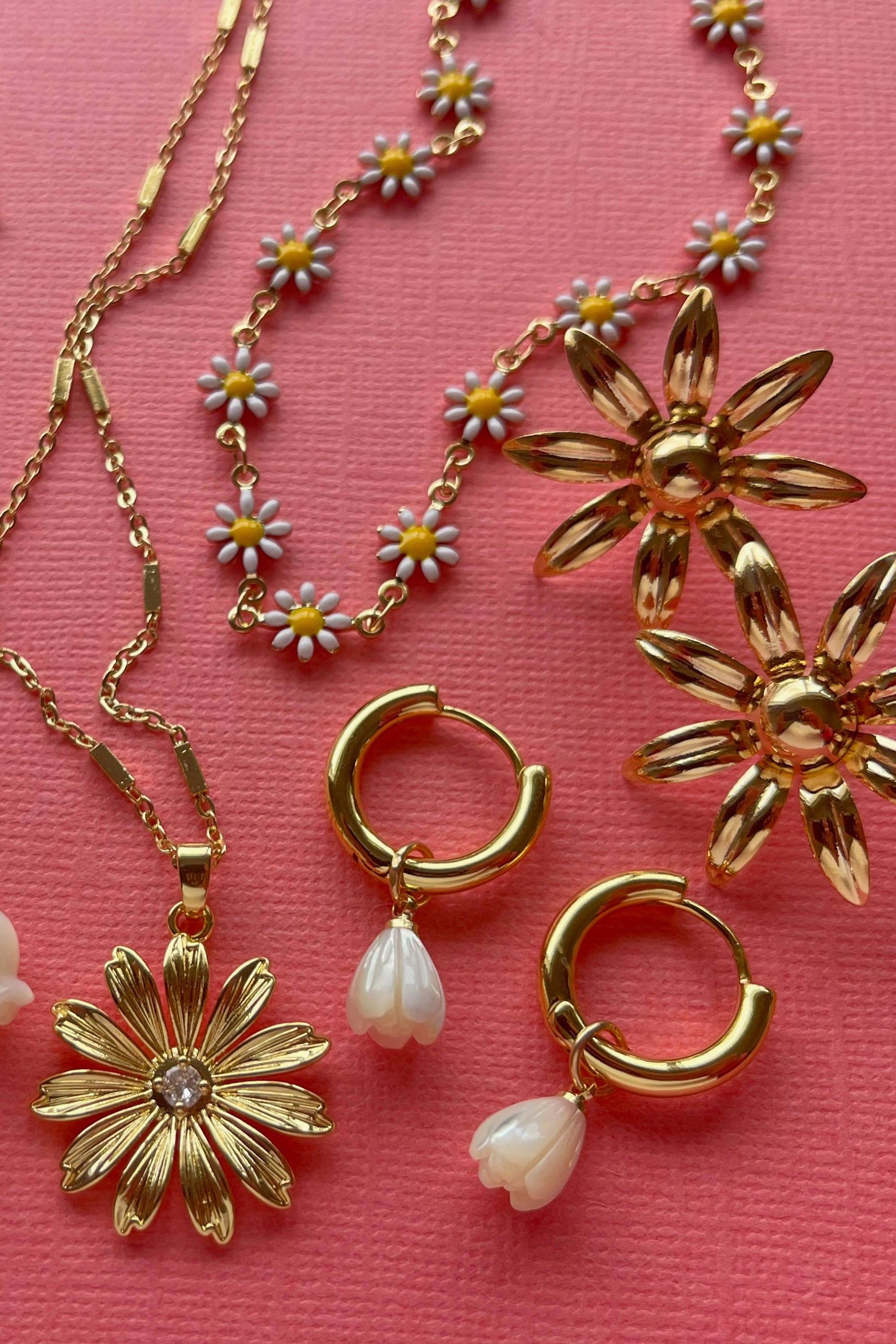 Gold jewelry including necklaces and earrings on a pink background