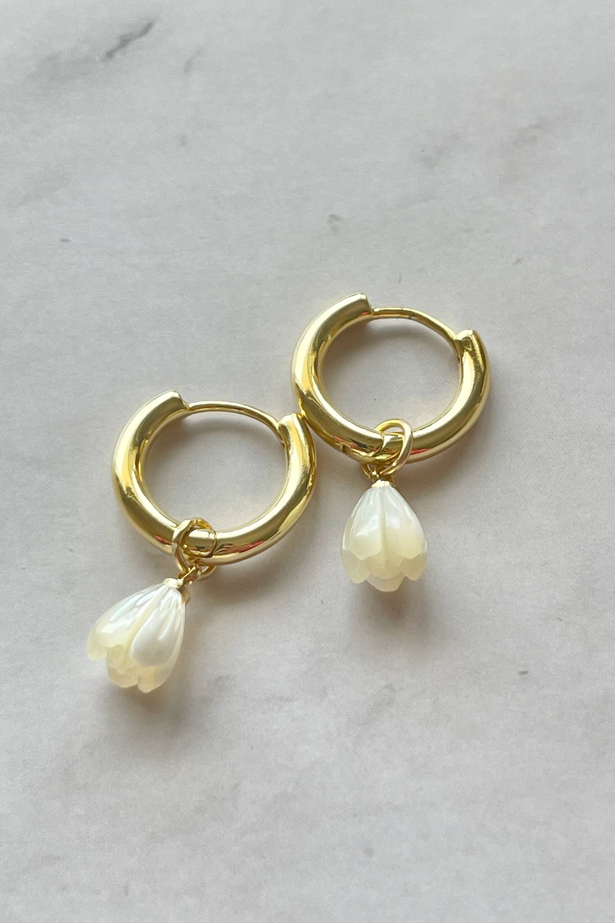 Gold hoop earrings with pearl drops on a marble surface