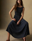 Woman wearing a black polka dot dress sitting against a beige background