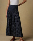 Woman wearing a white tank top and black patterned skirt on a beige background