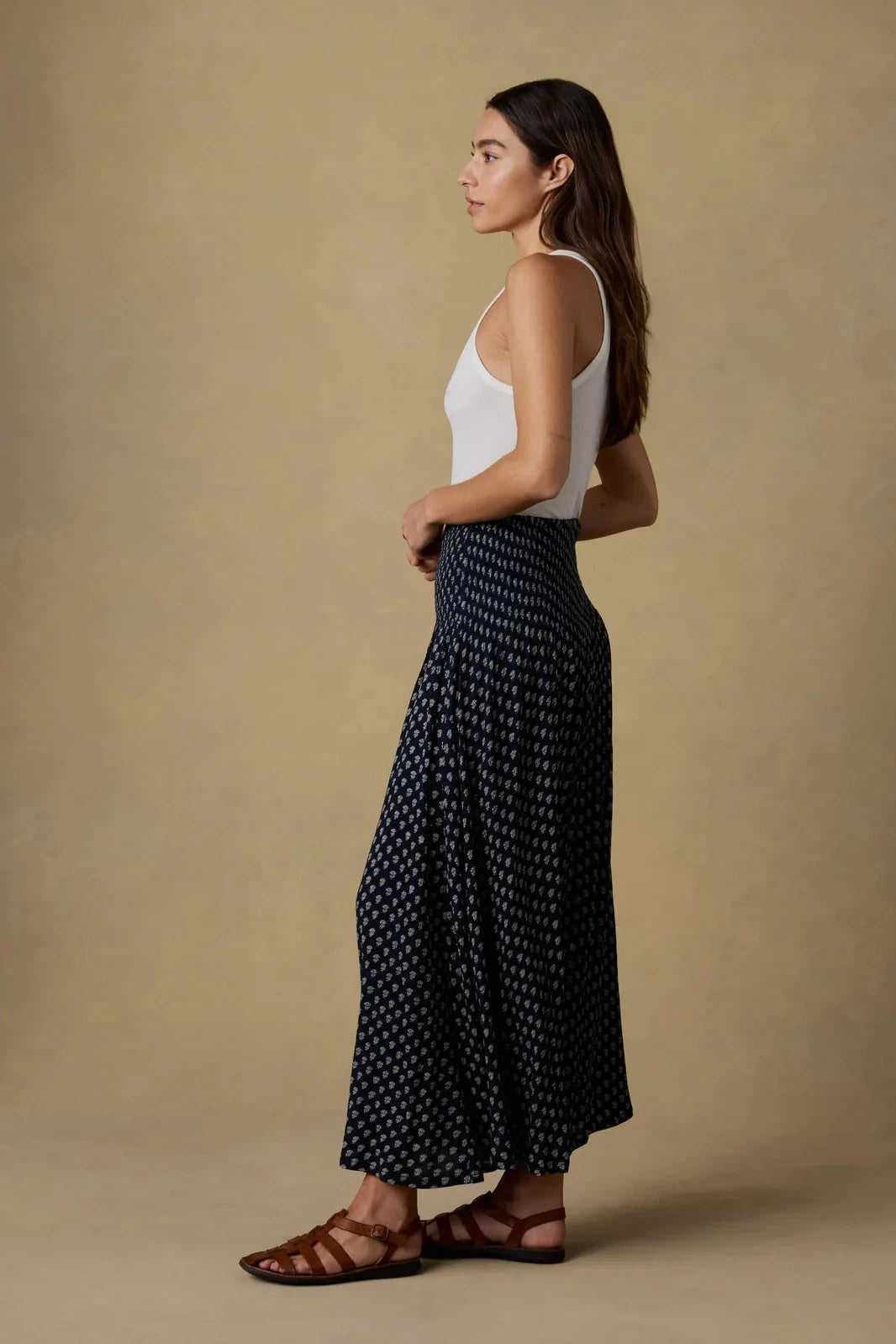 Woman wearing a white top and dark patterned pants against a beige background
