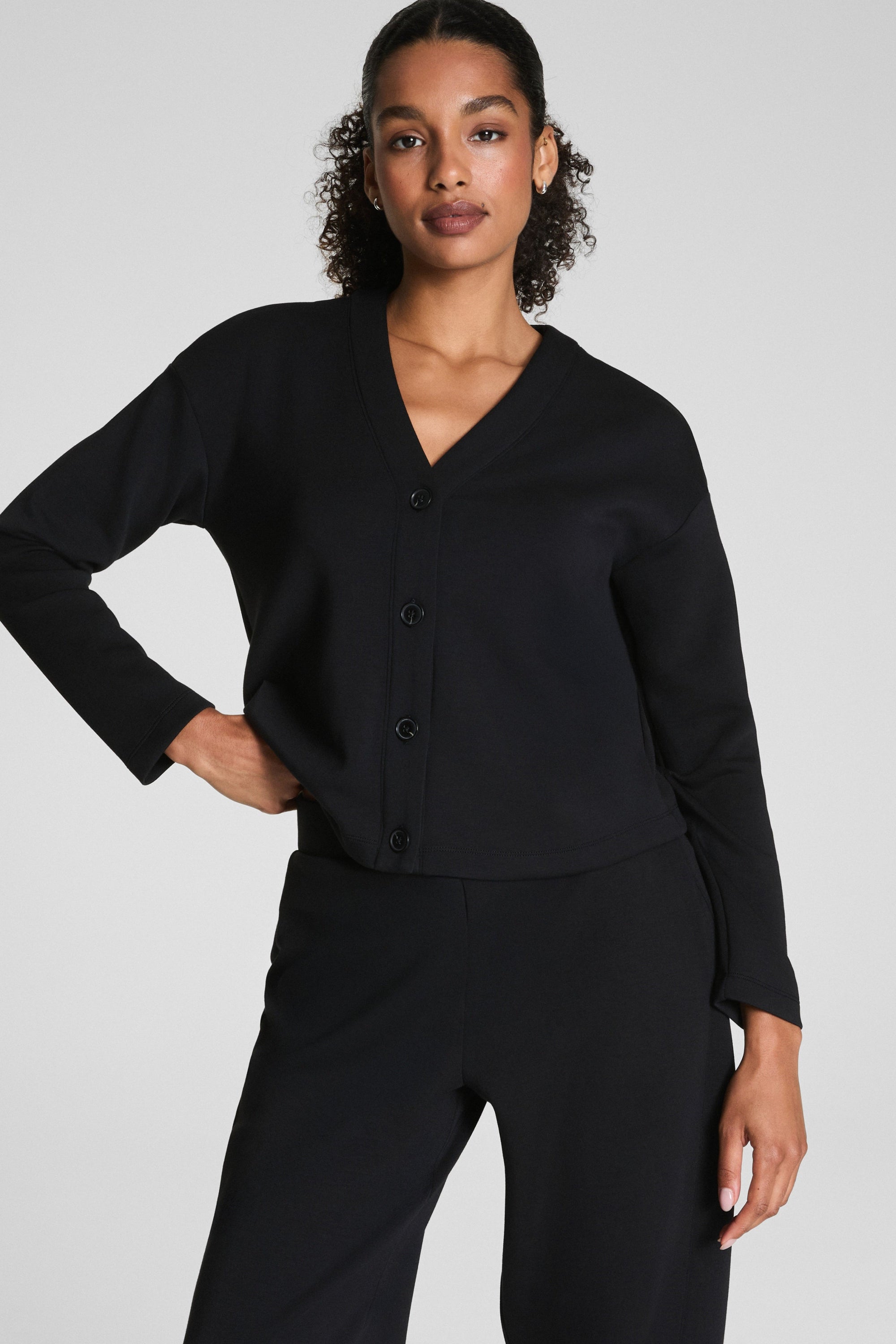 Woman wearing a black cardigan and pants on a light gray background