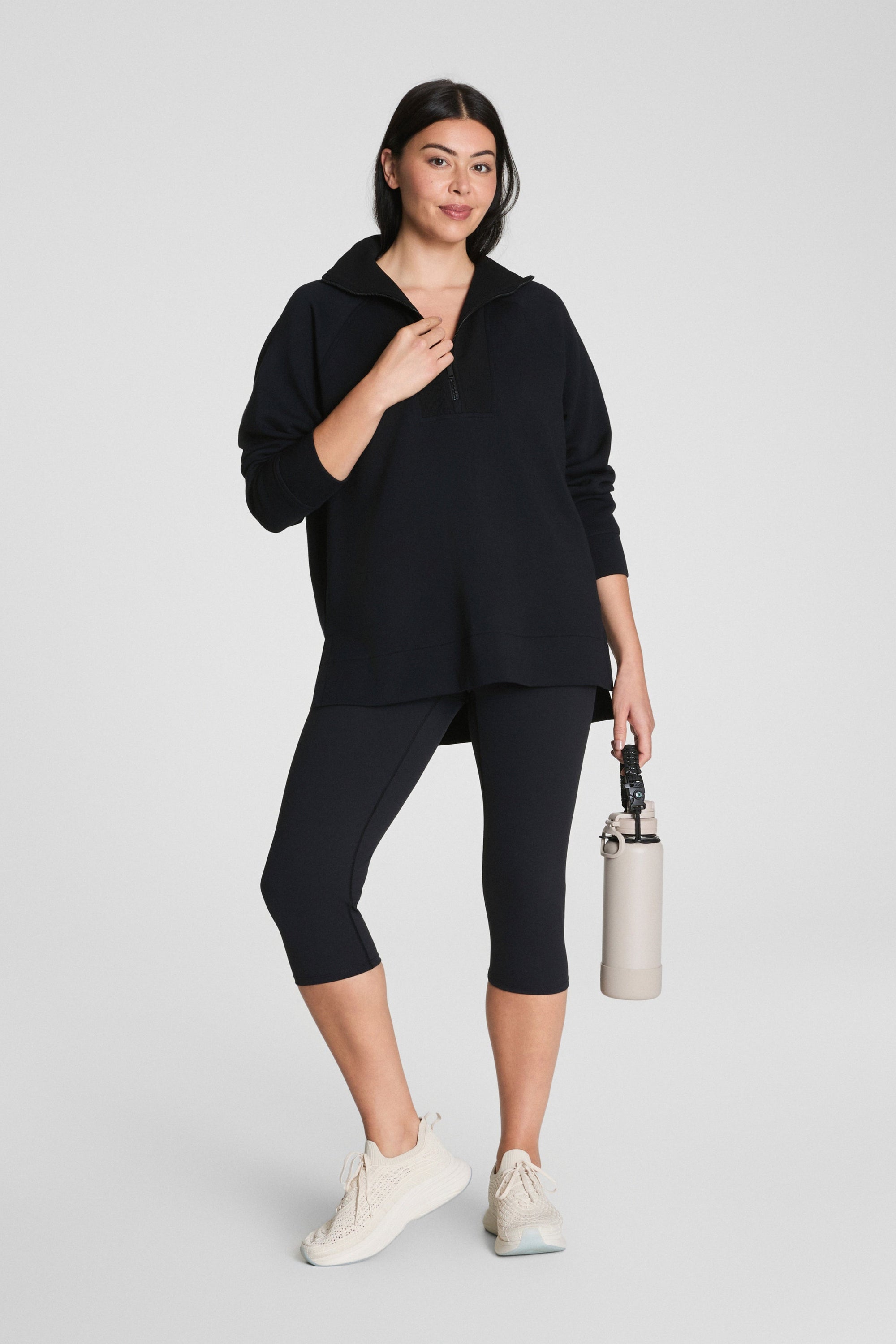 Woman wearing a black outfit holding a beige bag on a white background