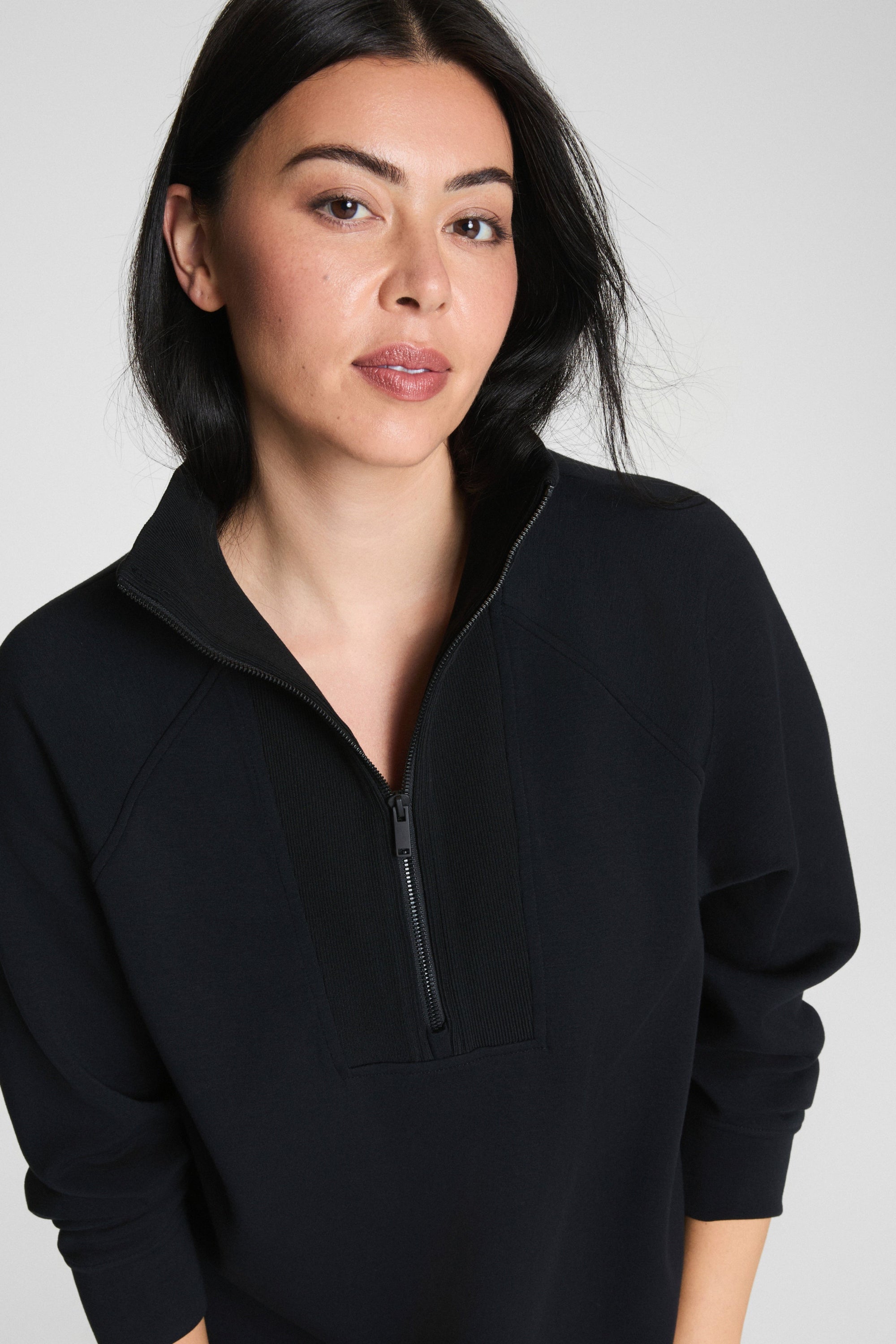 Woman wearing a black quarter-zip sweatshirt against a plain background