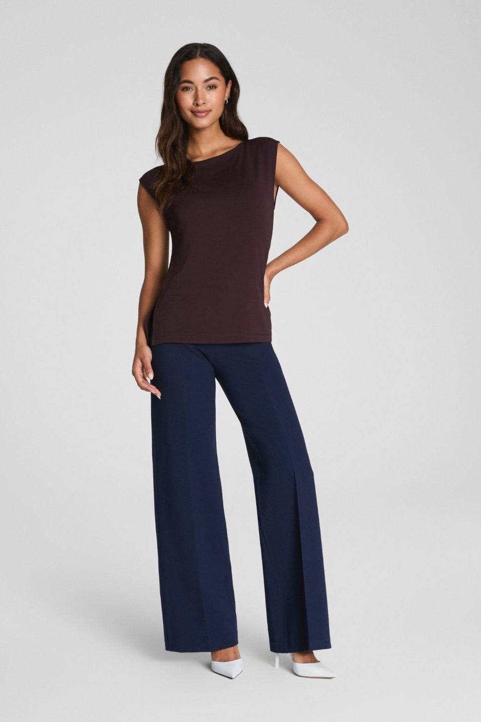 Woman wearing a brown sleeveless top and navy pants on a white background