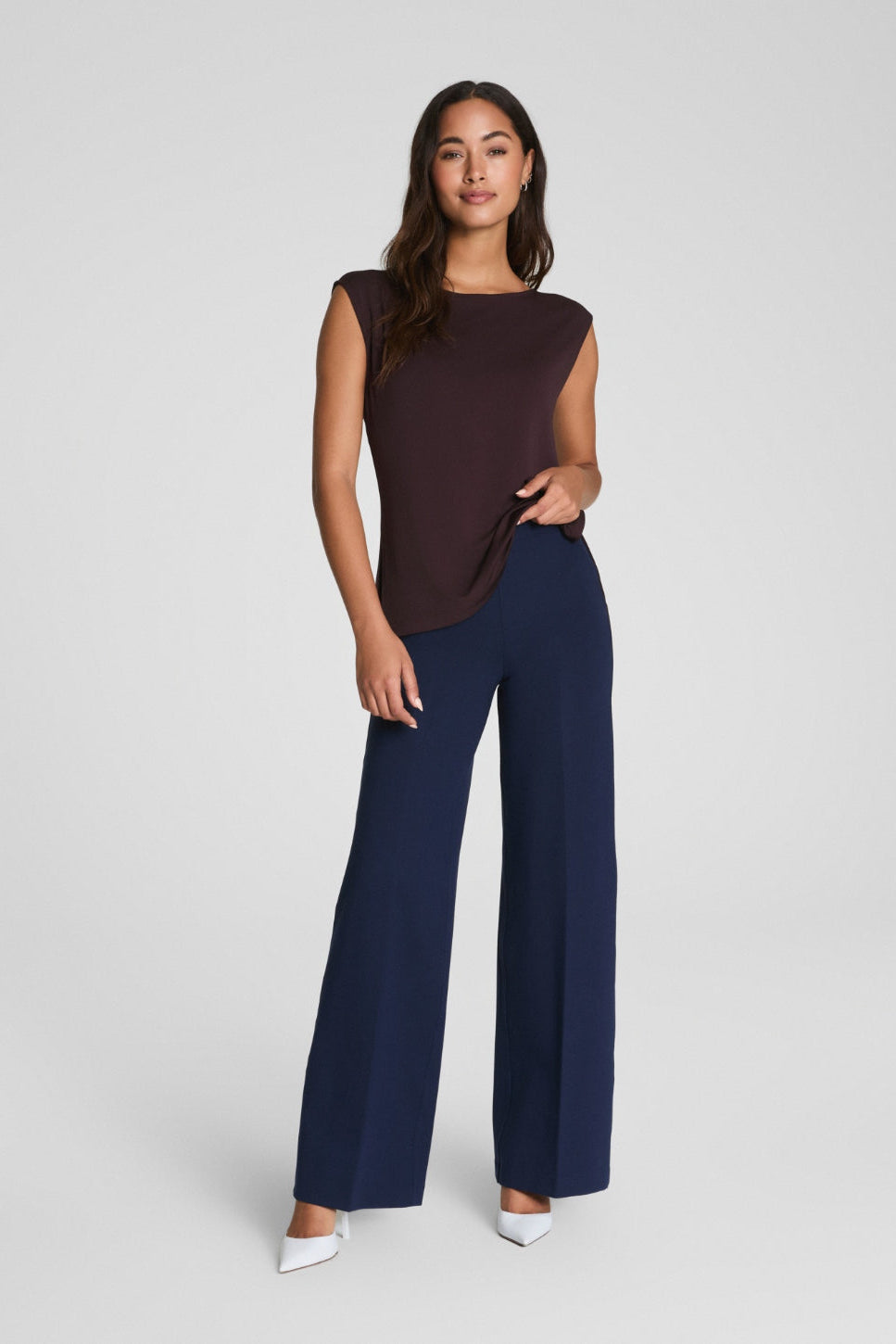 Woman wearing a brown top and navy pants on a white background