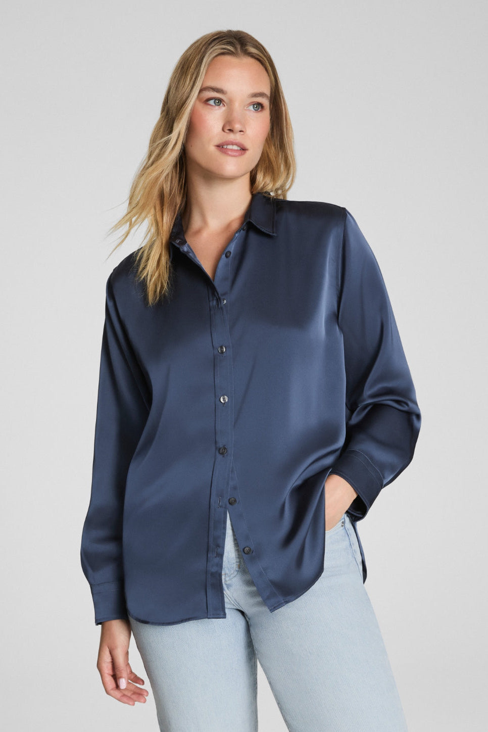 Woman wearing a navy blue shirt and light blue jeans against a gray background