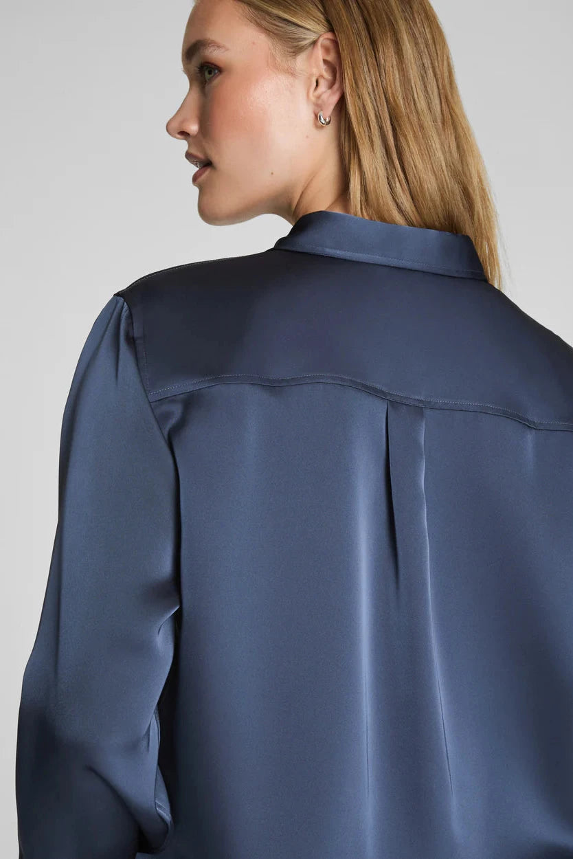 Person wearing a navy blue satin shirt on a plain background