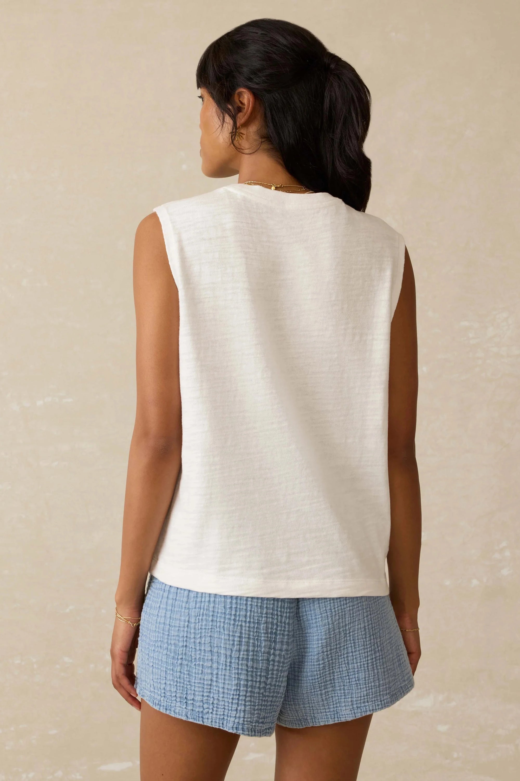 Woman wearing a white sleeveless top and blue shorts on a beige background