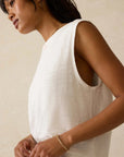 Woman wearing a white sleeveless top against a beige background