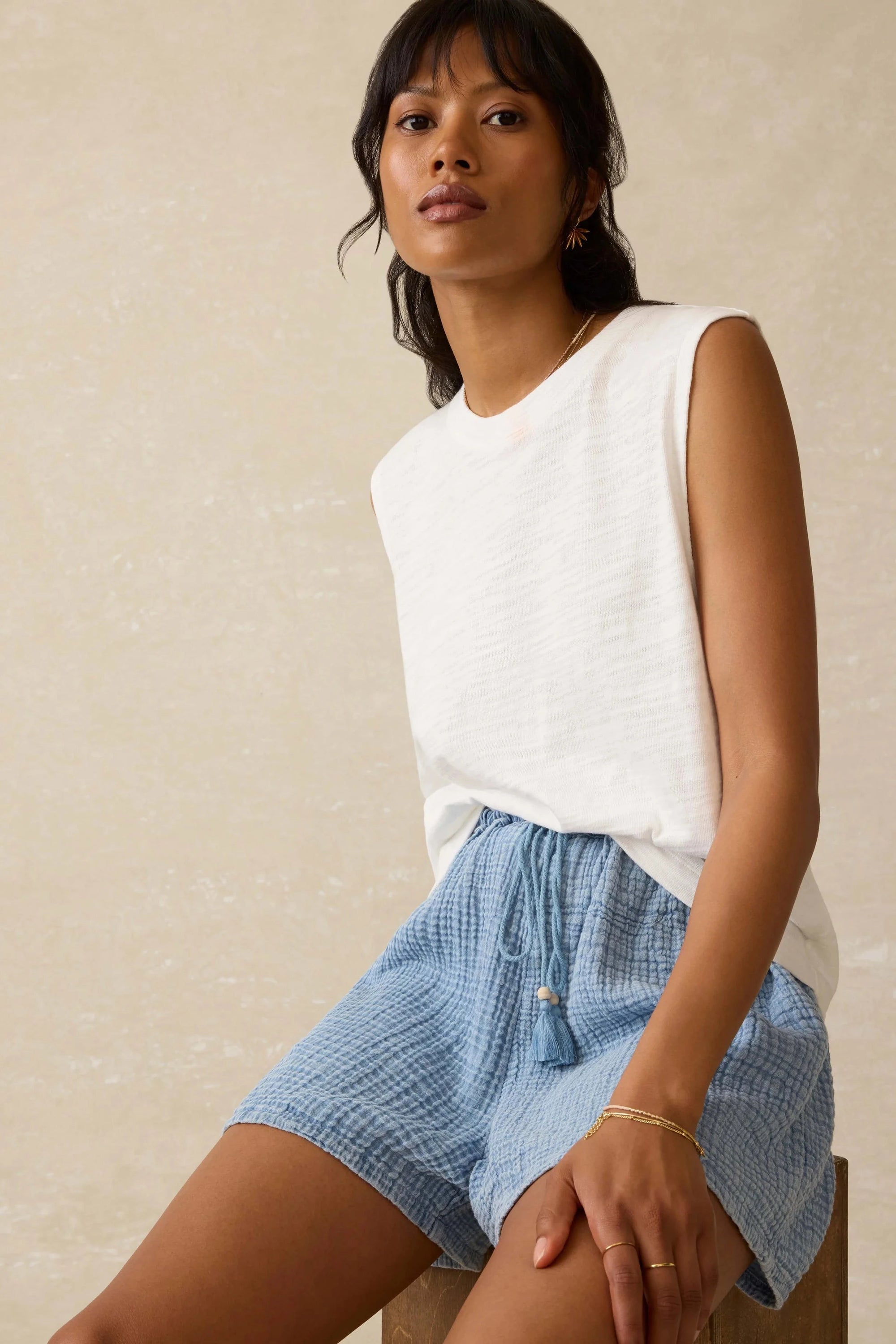 Woman wearing a white sleeveless top and blue shorts against a beige background