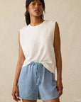 Woman wearing a white sleeveless top and blue checkered shorts on a beige background