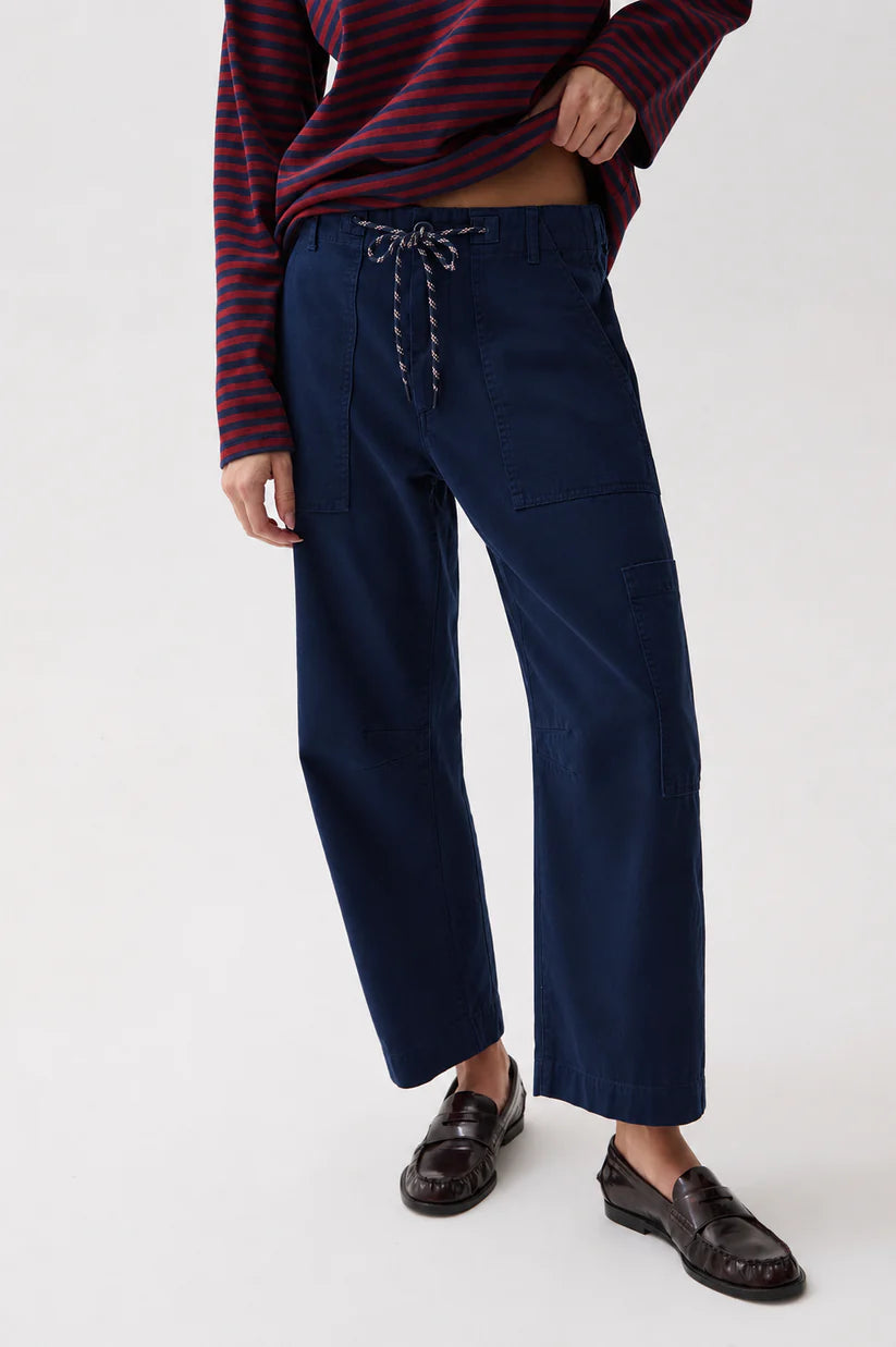 A person wearing navy wide-leg cropped pants with a drawstring waist, paired with a dark striped long-sleeve top and dark loafers, photographed against a clean light gray studio background.
