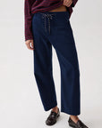 A person wearing navy wide-leg cropped pants with a drawstring waist, paired with a dark striped long-sleeve top and dark loafers, photographed against a clean light gray studio background.