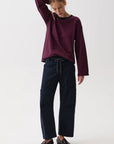 A woman modeling a dark red and navy blue horizontally striped long-sleeve top with dark navy wide-leg trousers and black leather loafers, standing against a plain white studio background.
