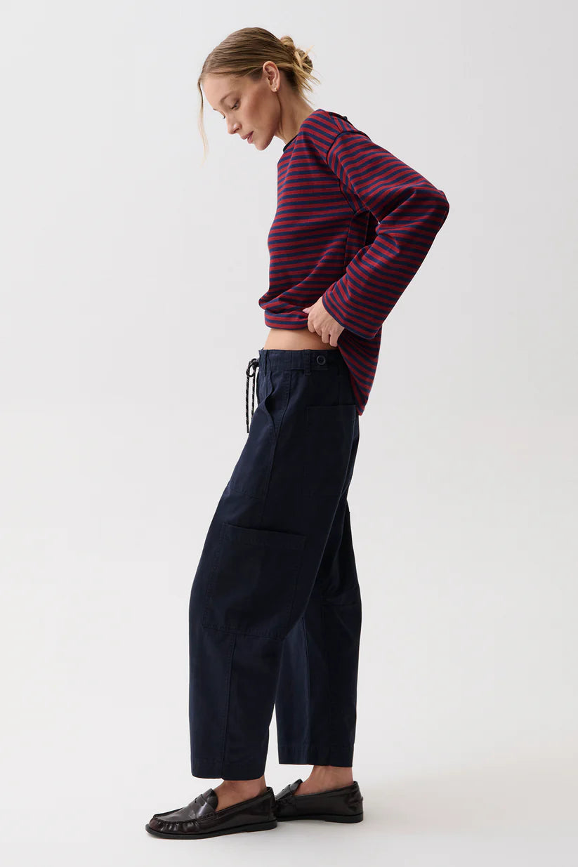A woman modeling a dark navy wide-leg cropped pants with a drawstring waist, paired with a burgundy and navy striped long-sleeve top and black loafers, against a plain white studio background.