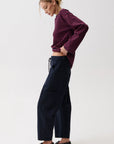 A woman modeling a dark navy wide-leg cropped pants with a drawstring waist, paired with a burgundy and navy striped long-sleeve top and black loafers, against a plain white studio background.