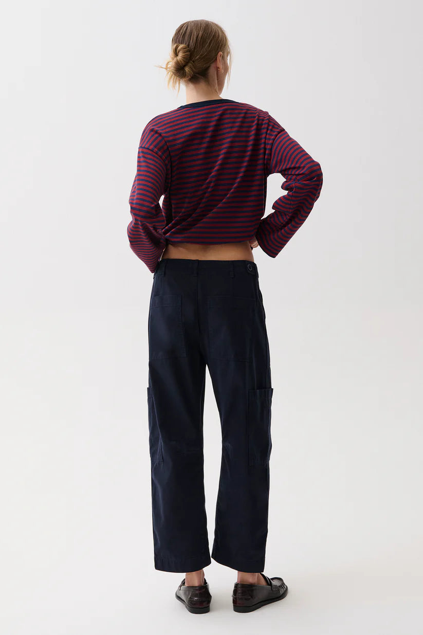 A model shown from the back wearing a cropped long-sleeve striped top in dark red and navy, paired with dark navy wide-leg pants and black shoes, against a plain white studio background.