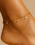 Gold anklet with small beads on a person's ankle against a beige background