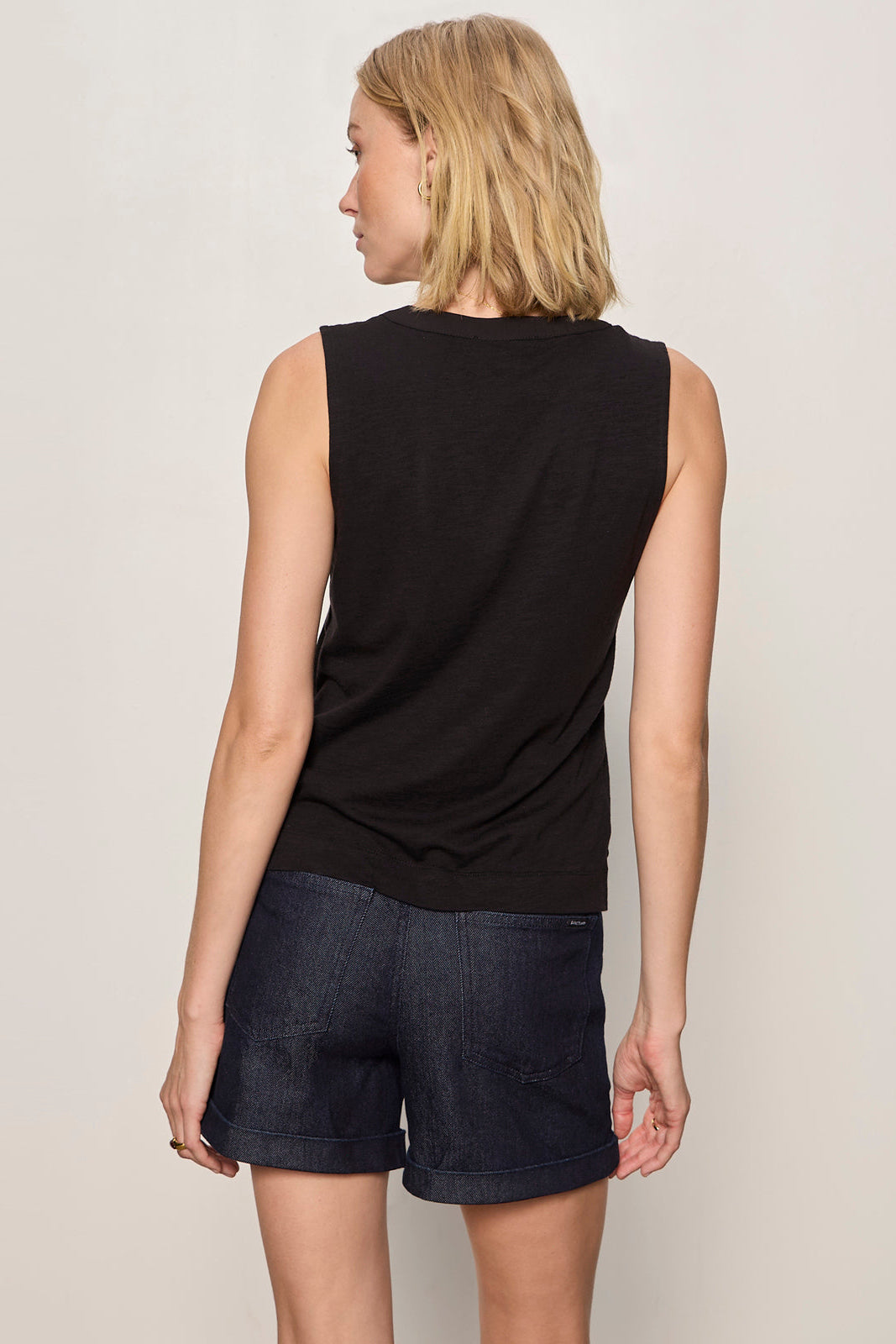 Woman wearing a black sleeveless top and dark shorts on a plain background