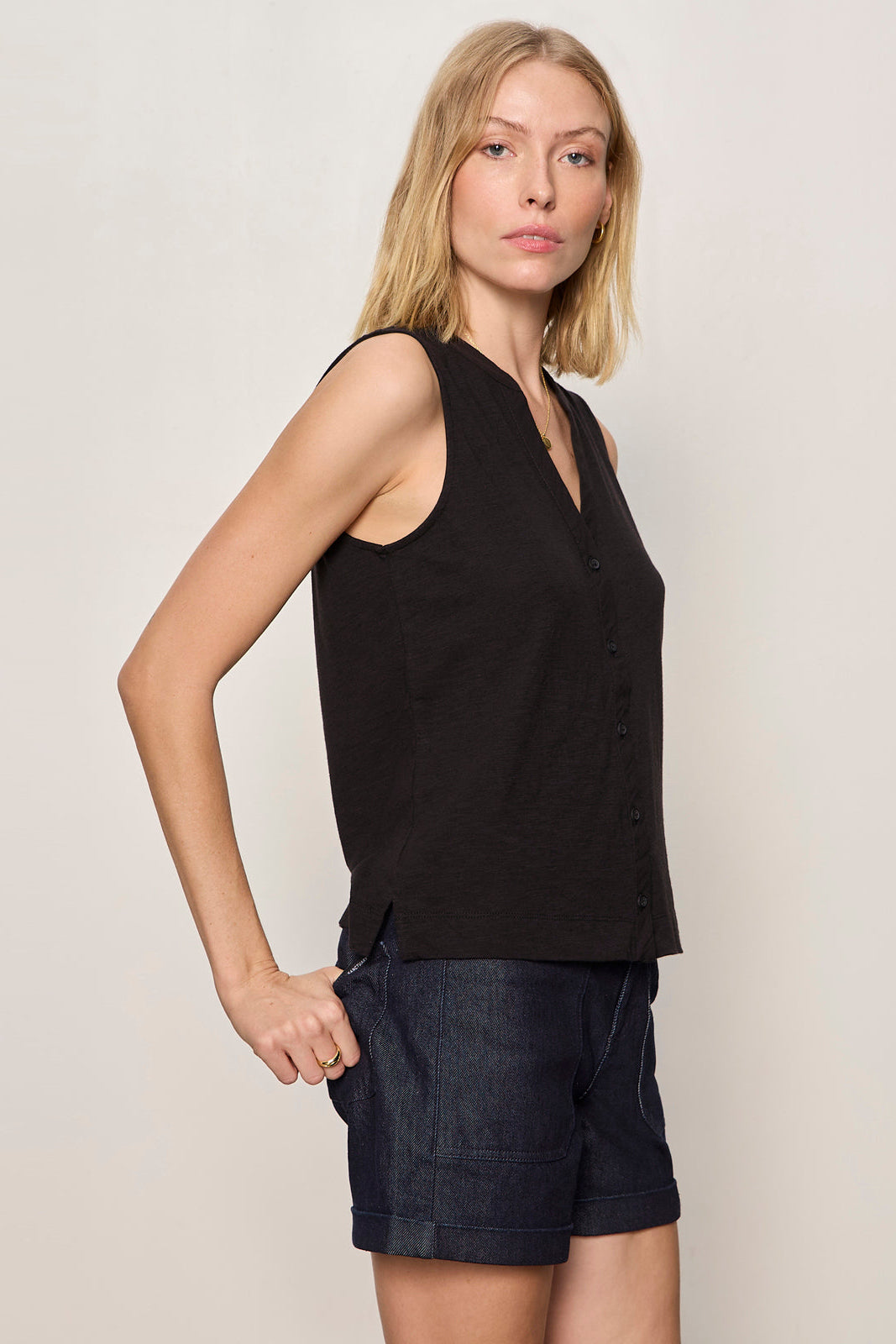 Woman wearing a black sleeveless top and dark shorts against a plain background