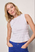 Woman wearing a white sleeveless top and blue pants against a plain background