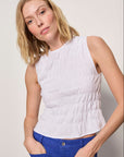Woman wearing a white sleeveless top and blue pants against a plain background