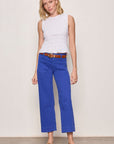 Woman wearing a white sleeveless top and blue pants against a plain background