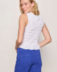 Woman wearing a white sleeveless top and blue pants against a plain background