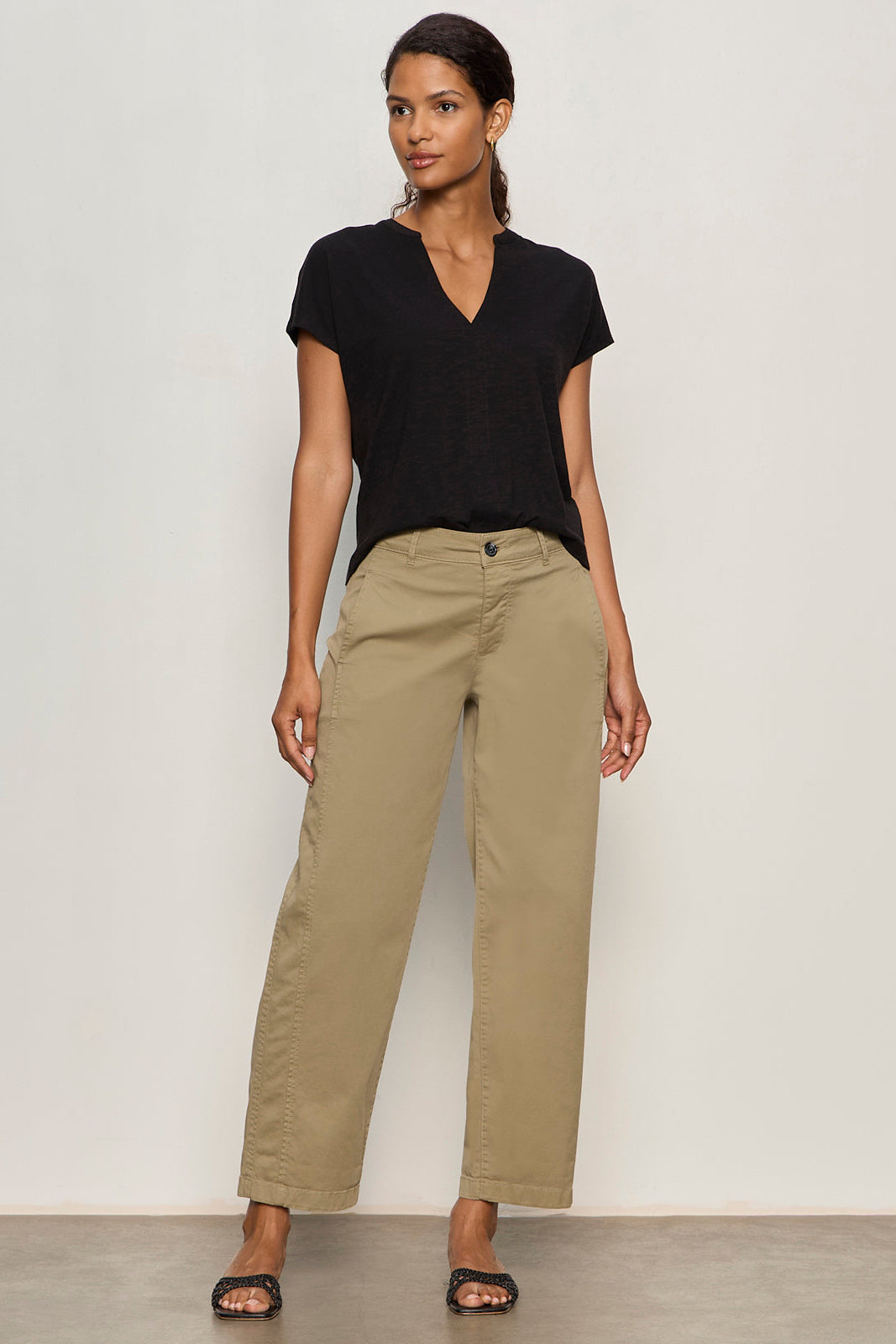 Woman wearing a black top and beige pants against a plain background