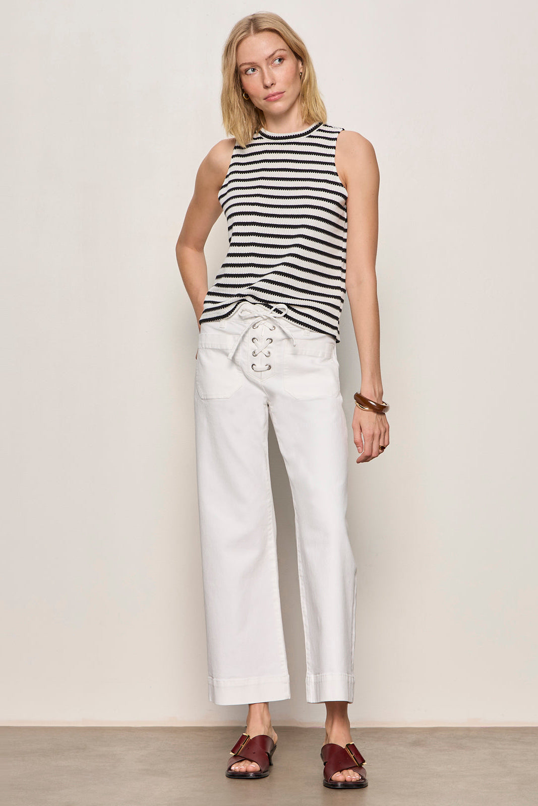 Woman wearing a black and white striped sleeveless top and white pants against a plain background