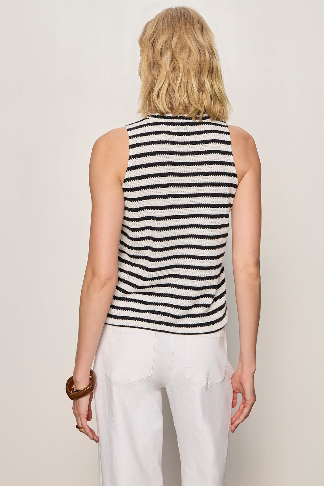Woman wearing a black and white striped sleeveless top with white pants on a plain background