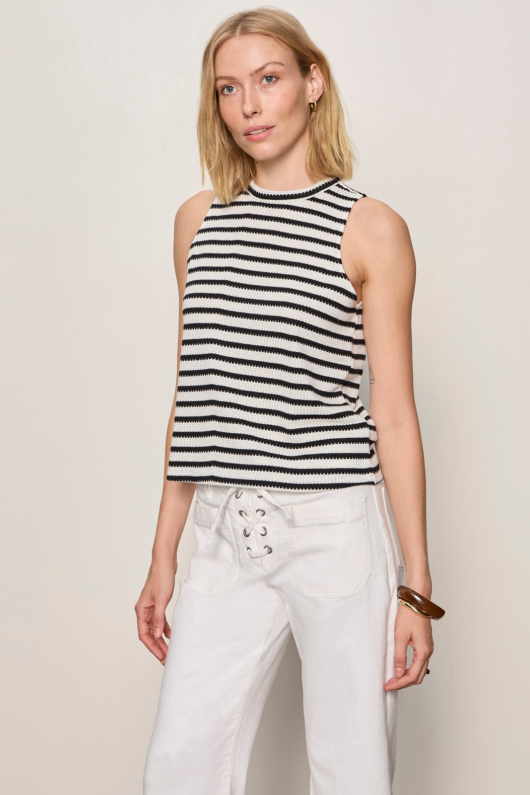 Woman wearing a black and white striped sleeveless top and white pants against a plain background