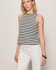 Woman wearing a black and white striped sleeveless top and white pants against a plain background