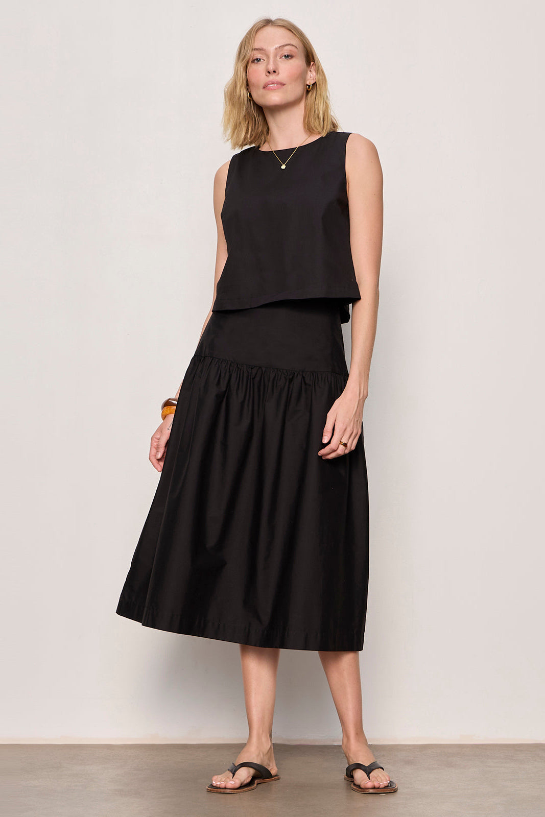 Woman wearing a black sleeveless top and skirt against a plain background